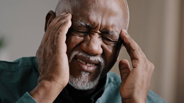 Крупным планом лицо грустный пожилой африканский американец испытывает головную боль хроническая мигрень нездоровый многорасовый дедушка массирует виски нездоровый 60-летний мужчина в отставке, страдающий высоким кровяным давлением - Фото, изображение