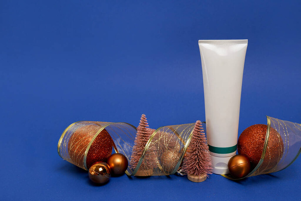 Tubo de crema cosmética con decoraciones navideñas sobre fondo azul con espacio para copiar - Foto, imagen