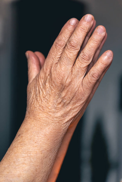 Ruce staré ženy složené k modlitbě na rozmazaném pozadí, koncept víry v Boha a náboženství. - Fotografie, Obrázek