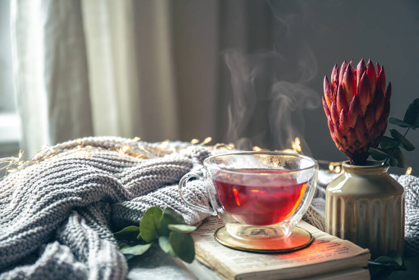 Eine gemütliche Komposition mit rotem Tee, einer Blume und einem Strickelement auf verschwommenem Hintergrund, Kopierraum. - Foto, Bild