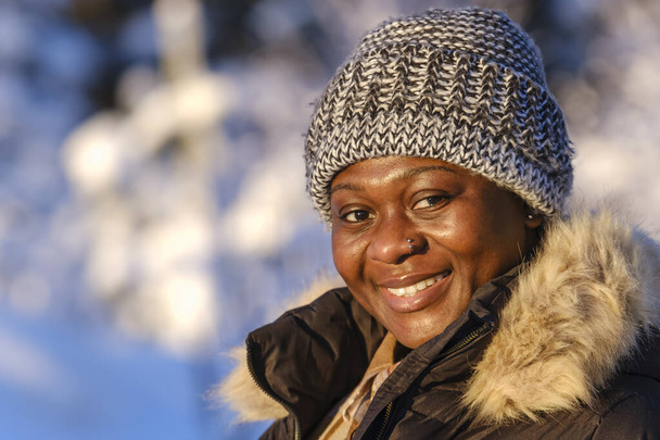 Mujer africana afuera durante un día de invierno frío y soleado en la naturaleza sueca. - Foto, imagen