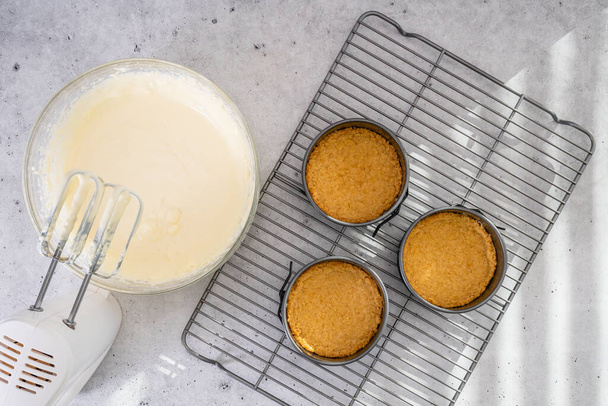 Sajttorta recept. Három mini kerek torta serpenyő (ón, penész), zúzott keksszel, és sajttorta tészta egy tálban, lapos tojással - Fotó, kép
