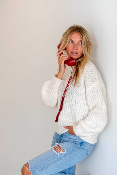 Шикарная блондинка-модель разговаривает по телефону, демонстрируя эмоции в домашней обстановке - Фото, изображение