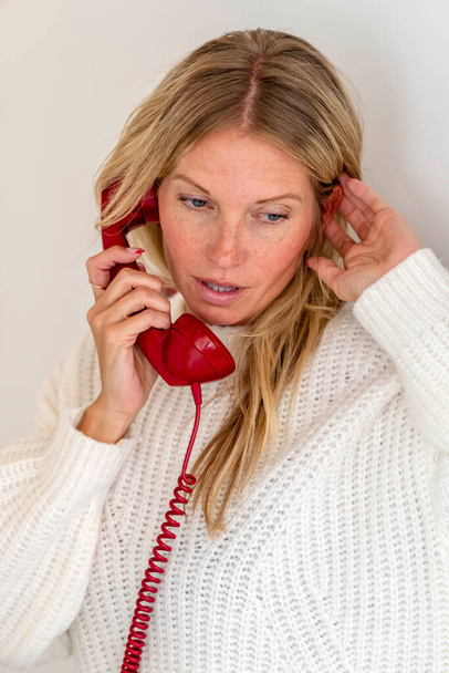 A gorgeous blonde model talks on the phone showing emotion in a home environment - Photo, Image