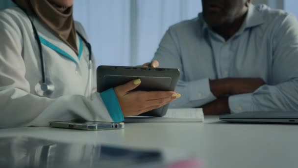 Молодая женщина врач в хиджабе медсестра использовать электронный цифровой планшет показать результаты тестов на здоровье на веб-экране для африканского пожилого человека пациента слушать профессиональные рекомендации обсудить лечение - Кадры, видео