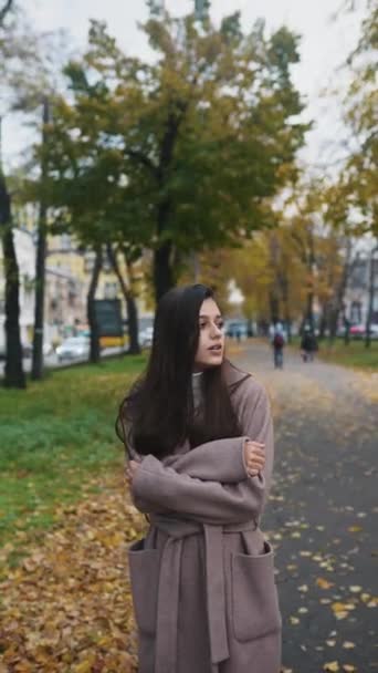 Nuori nainen syksyllä takki yrittää pysyä lämpimänä kadulla - Materiaali, video