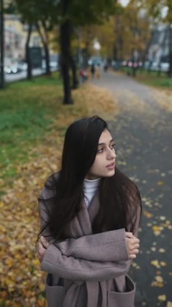 Eine junge Frau im Herbstmantel versucht sich auf der Straße warm zu halten - Filmmaterial, Video