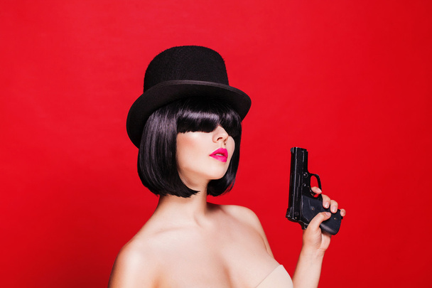 fashion beautiful model with pistol in hat cylinder, on red background - Foto, imagen