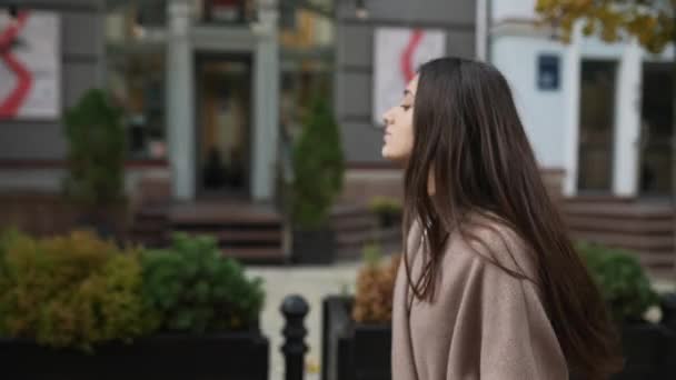 Μια νεαρή γυναίκα με φθινοπωρινό παλτό περπατά στην πόλη. - Πλάνα, βίντεο
