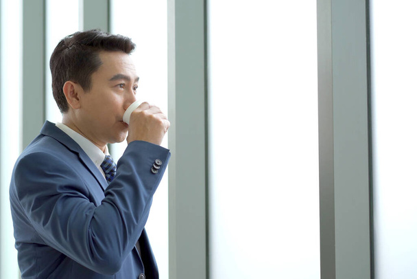 Smart and good looking Asian businessman relaxing and drinking a coffee, senior manager drinking a coffee during a coffee break in afternoon. Photograph with copyspace. - Photo, Image