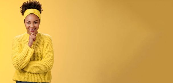 Enthousiaste creatieve goed uitziende zwarte jonge vrouw dragen trui hoofdband uitstekend plan glimlachen tevreden blij kijken doordachte camera make-up idee, staande gele achtergrond. - Foto, afbeelding