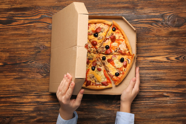 Női kéz doboz ízletes pizza fa háttér - Fotó, kép