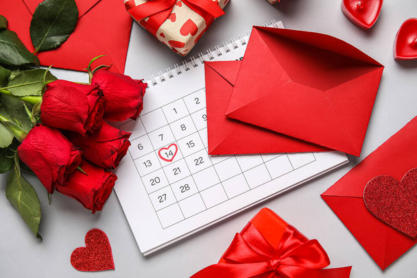 Ημερολόγιο με την ημερομηνία της ημέρας του Αγίου Βαλεντίνου, φάκελοι, τριαντάφυλλα και δώρα στο γκρι φόντο - Φωτογραφία, εικόνα