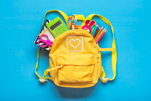 Back to school, education concept Yellow backpack with school supplies - notebook, pens, eraser rainbow, numbers isolated on blue background Top view Copy space Flat lay composition Banner. - Photo, Image