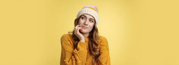 Мечтательная творческая очаровательная девушка в тёплом свитере в шляпе, смотрящая на вдумчивое романтическое свидание, счастливо улыбаясь, представляя, как она вспоминает прекрасные воспоминания, стоя на восхитительном желтом фоне. - Фото, изображение