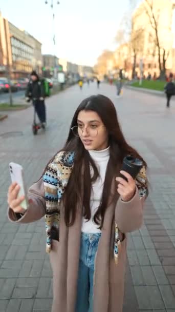 Szczęśliwa uśmiechnięta młoda kobieta dzwoniąca wideo na zewnątrz w mieście. Stylowe kobiety podróżnik biorąc selfie lub wideo na blogu internetowym. - Materiał filmowy, wideo