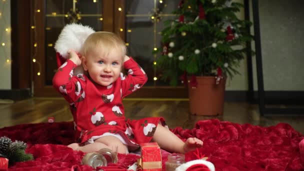Belle petite fille d'un an aux cheveux blonds jouant au chapeau de Noël, aux enfants et à la veille du Nouvel An. - Séquence, vidéo