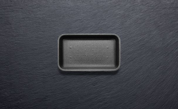 vassoio di polistirolo nero contro una piastra di ardesia nera dall'alto - Foto, immagini