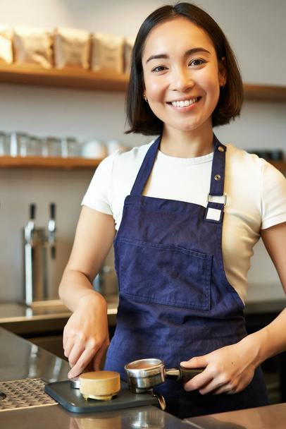 Vertical tiro de barista, menina asiática no café usando adulteração para máquina de café, vestindo avental azul, preparando a ordem. - Foto, Imagem