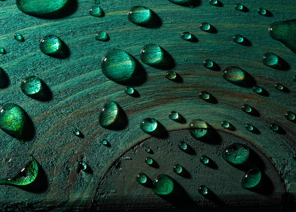 Fresh rain water droplets on green wood table closeup view. - Photo, Image