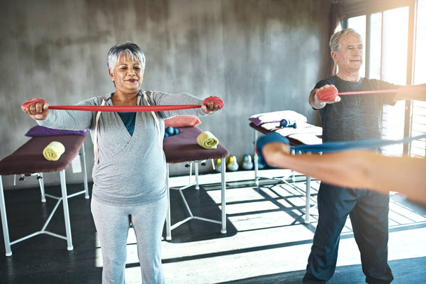 Good health is important at any age. a senior man and woman using resistance bands with the help of a physical therapist - Fotografie, Obrázek
