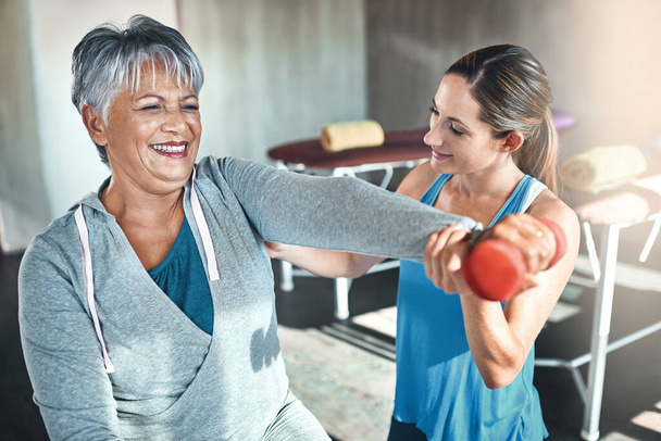 Word fit en heb plezier terwijl je het doet. een oudere vrouw met gewichten en een fitnessbal met behulp van een fysiotherapeut - Foto, afbeelding