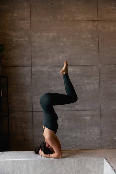 Jeune femme sportive et séduisante pratiquant le yoga, faisant de l'exercice de la tête, variation de la pose de salamba sirsasana, s'entraînant, portant des vêtements de sport, haut gris, vue rapprochée intérieure, studio de yoga, vue arrière
 - Photo, image