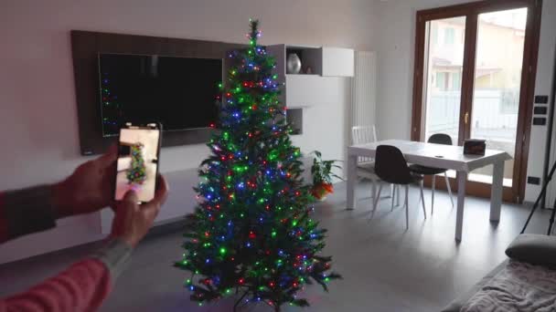 Uomo che utilizza l'app Smart Home per decorare e illuminare l'albero di Natale. Vista posteriore. - Filmati, video