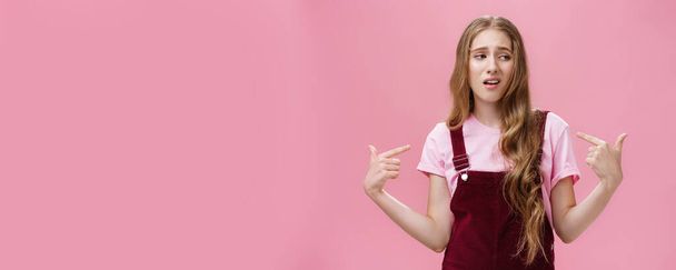 Self-assured arrogant young female student with high ego standing cocky and brag about herself pointing at her with cool snobbish look looking away to right with contempt posing over pink wall. Body - Photo, Image