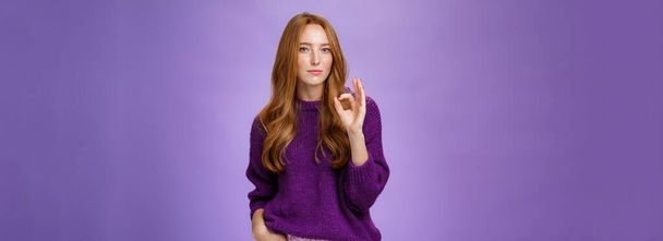 Buen trabajo, genial. Retrato de mujer pelirroja encantadora elegante y segura de sí misma en suéter púrpura que muestra un gesto aceptable como reacción a un excelente trabajo, orgullosa de su amigo sobre la pared violeta. - Foto, Imagen