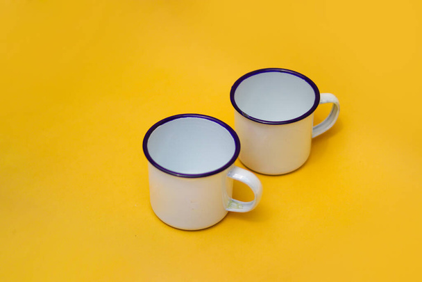Two white mugs on orange background. Enameled white mug, stainless mug, camping mug. - Photo, Image