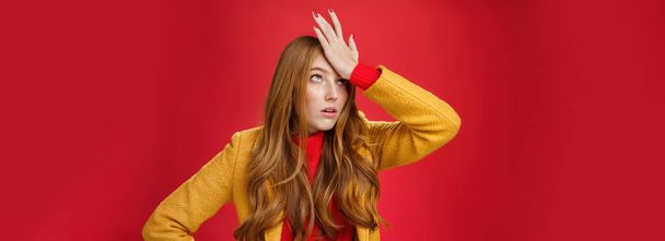 Redhead businesswoman making facepalm gesture with hand on forehead rolling eyes up from annoyance and irritation as being shocked with how dumb client is sighing bothered over red wall, tired. - Fotografie, Obrázek