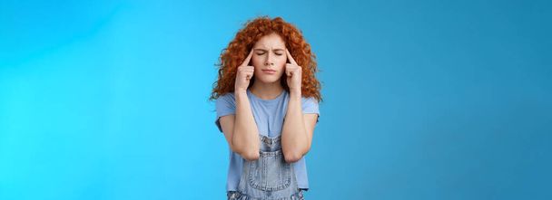 Come on girl think. Perplexed distressed concerned intense redhead curly woman close eyes frowning touch temples suffer migraine painful headache cannot concentrate blue background. Copy space - Photo, Image
