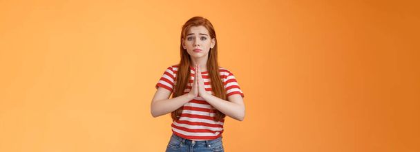 Silly redhead innocent girl acting pity, pulling sad face begging for help, hold hands pray, frowning, purse lips upset, plead favor, apologizing, saying sorry, stand orange background in need. - Photo, Image