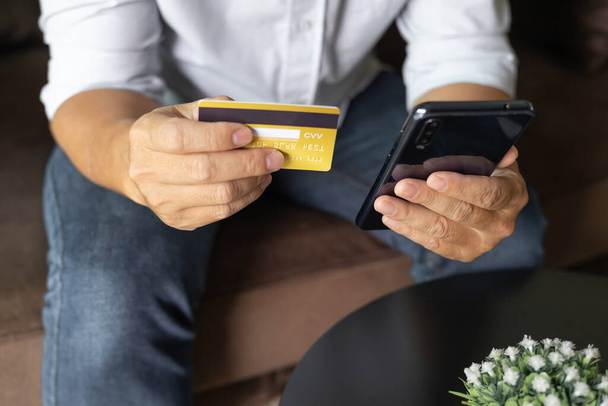 Man holding credit card and using smartphone at home, businessman shopping online, e-commerce, internet banking, spending money, working from home concept, Sit on the sofa in the living room at home. - Photo, Image
