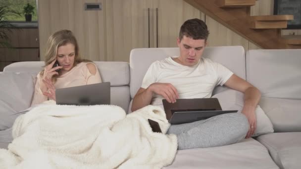 閉め出す隔離中に自宅で働いている若い夫婦が忙しいです。自宅から仕事をしようとしているパートナー間の迷惑の優しい覚醒。家庭で現代的なワイヤレスデバイスを使用している2人の大人 - 映像、動画