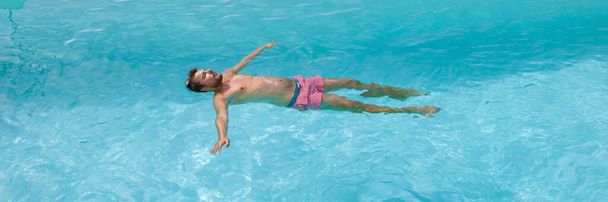 hombres caucásicos jóvenes flotando en una piscina azul durante el verano.  - Foto, Imagen