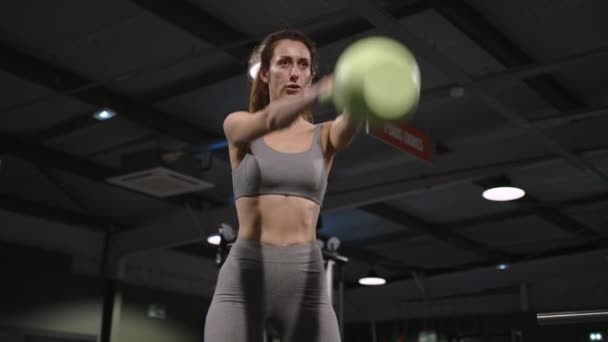 Mulher atraente em sportswear levanta um kettlebell de esportes e agachamentos na luz de fundo. Imagens 4k de alta qualidade - Filmagem, Vídeo