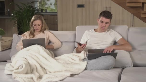 CLOSE UP: Couple using laptops and smartphones for remote work in home isolation. Married couple making business calls and other office work from their home couch office while being in quarantine. - Footage, Video