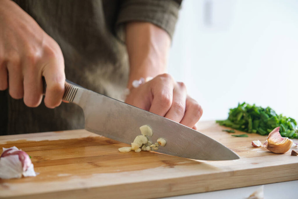 Крупным планом азиатского молодого человека руки режут чеснок на кухне. - Фото, изображение