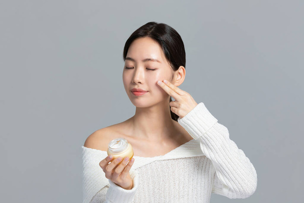 beautiful young Korean Asian woman portrait studio photo in winter skin beauty and cosmetics concept, holding a nutritional cream - Fotoğraf, Görsel