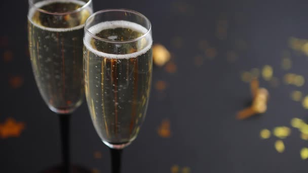 Twee glazen sprankelende champagnewijn met gouden decoratie van confetti en serpentines op zwarte elegante achtergrond. Bovenaanzicht met kopieerruimte. Feestelijk of partijconcept. - Video