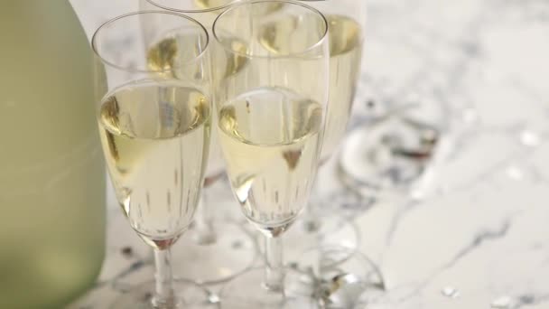 Шампанські окуляри та пляшки розміщені на білому мармуровому фоні. Концепція вечірнього та святкового святкування з конфетті та зміями. За допомогою простору копіювання
. - Кадри, відео