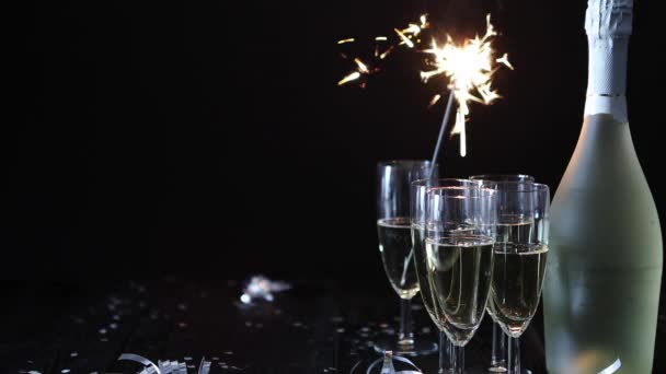 Party composition image. Glasses filled with champagne placed on black table. With bottle of wine and sparkler. Elegant composition with copy space. - Footage, Video
