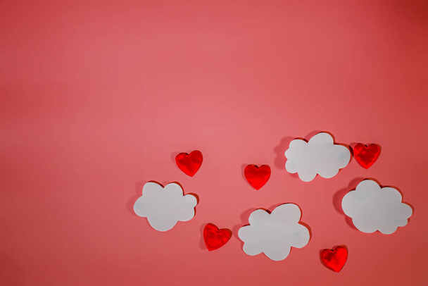 Witte papieren wolken en rode textielhartjes op een rode achtergrond. Conceptuele achtergrond voor Valentijnsdag of Vrouwendag. Kopieerruimte. - Foto, afbeelding
