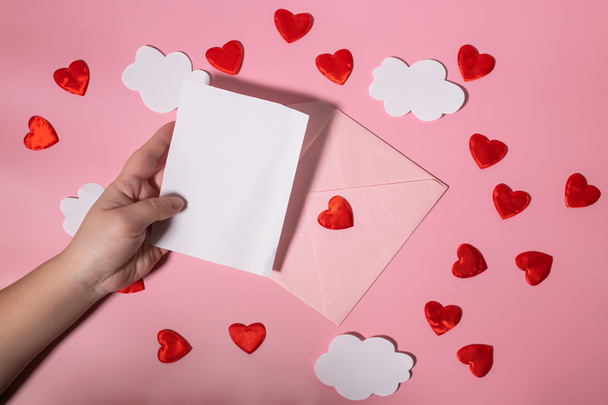 Kézen fogva egy üres levél nyomtatványt Valentin napra vagy anyák napjára egy szívekkel teli borítékon. Mockup - Fotó, kép