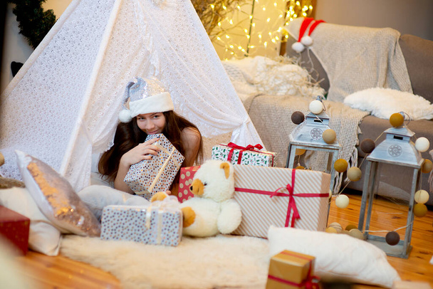 Όμορφη γυναίκα κορίτσι ξαπλωμένη σε χριστουγεννιάτικα δώρα φορούν ασημί χρώμα Σάντα καπέλο, vintage στυλ διακοσμημένο σπίτι σαλόνι - Φωτογραφία, εικόνα