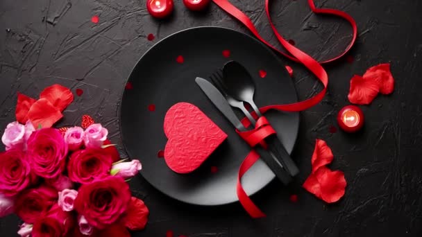 Valentijnsdag, de instelling van de tabel en romantisch diner concept. Close up van de plaat met bestek en rozenblaadjes op zwarte stenen achtergrond - Video