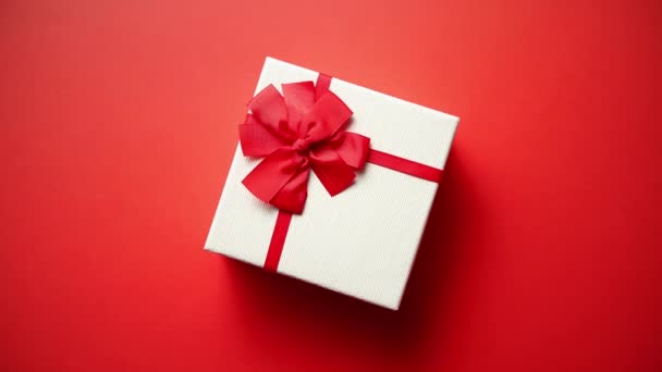 Draufsicht auf Geschenk in gestreiftem Geschenkpapier verpackt mit Band auf rotem Papier Hintergrund dekoriert. Valentinstag, Weihnachten oder Geburtstag und Feier Konzept - Filmmaterial, Video