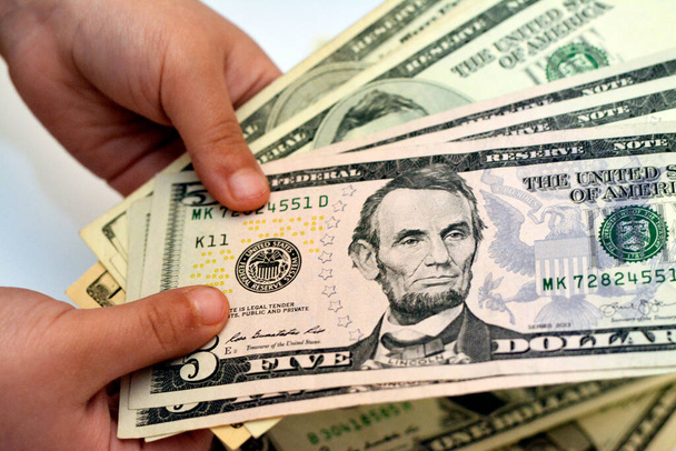 Fünf 5-Dollar-Banknoten in der Hand eines kleinen Kindes zeigen das Profil eines Porträts von Abraham Lincoln, dem 16. US-Präsidenten, Wirtschafts- und Finanzkonzept für die Zukunft - Foto, Bild